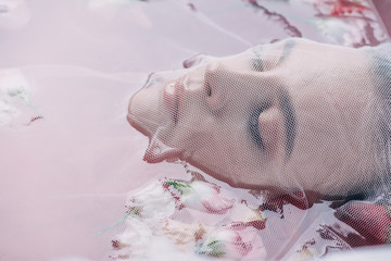 close up view of beautiful woman covered with white mesh cloth in pink water with rose petals