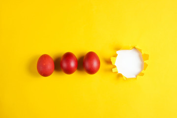 Red chicken eggs on a yellow paper background with a torn hole for copy space. Top view. Minimalism Easter concept