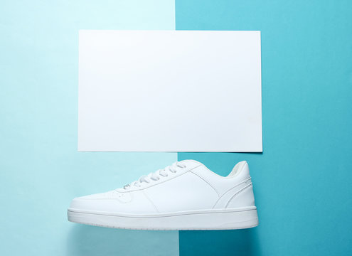 White Sneaker On A Blue Background With A White Sheet Of Paper For Copy Space, Top View