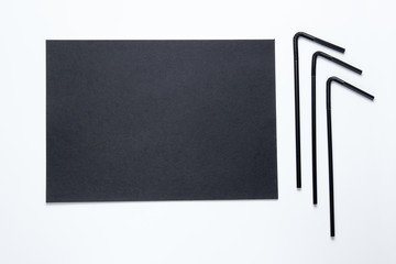 Black cocktail tubules and a black sheet of paper for copy space on a white background. Top view