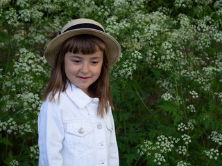 А pretty little girl is picking flowers. A sunny child in a straw hat is picking dandelions on a green glade. Summer girl.