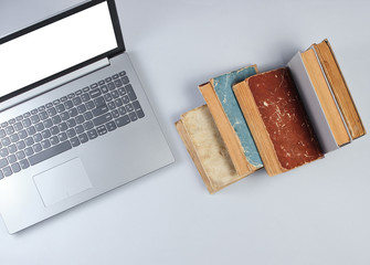 Modern laptop and many old books on a gray background. Old and new sources of information. Top view