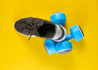 Sports sneakers and dumbbells on yellow background. Fitness concept