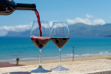 Waiter pouring red wine in wine glasses on outdoor terrace witn blue sea and mountains view on background