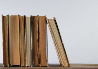 Stack of old books on woden shelf against the background of a white wall