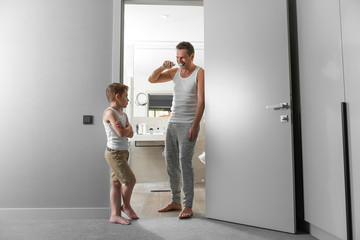 Happy dad and smiling son brushing their teeth near bathroom