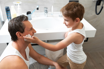 Father and son are standing in the bathroom and shaving