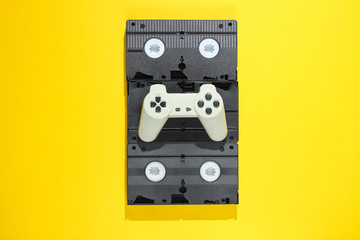 Gamepad on retro video cassettes. Minimalism studio shot on yellow background