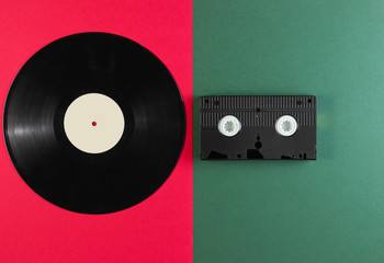 Vinyl record and video cassette on a green-red background. Retro style. Top view.