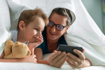 Happy father and son using smartphone in room