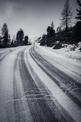 Obraz premium empty snowcapped road with car tracks in dramatic black and white foggy landscape mountain range in dolomites in wintertime, giau pass, italy