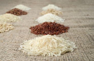 Few piles of rice of different varieties on the background of sacking. Selective focus.