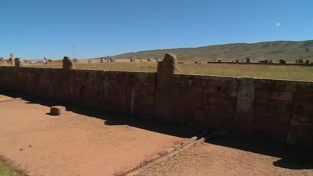 Medium high angle panning shot of part of Tiwanaku wall ruins with pieces of detached stones, drainage, and tourists visiting the site, Tiwanaku, La Paz, Bolivia
