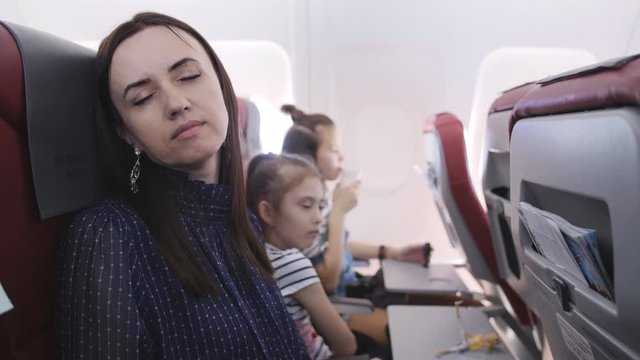 The family is flying to traveling by plane. A woman sleeps on the seat in front.