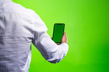 A man holds in his hand a smartphone on a green screen