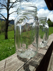 empty glass jars with handles, on wooden veranda, summer garden background. For refreshing homemade drink. Holiday countryside lifestyle concept. Close up view, natural daylight
