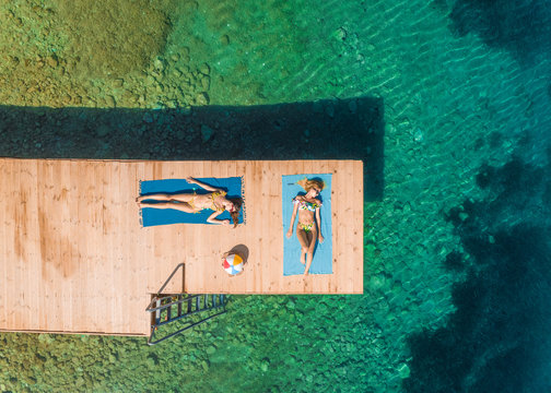 Aerial view of two attractive women sunbathing on wooden pontoon in Panagopoula, Greece.