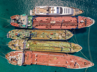 Aerial view of luxury yacht moored up with old cargo boats in the mediterranean sea, Nisi, Greece.