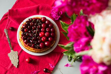 Homemade pie with fresh cherry and plums on linen tablecloth with bouquet of peonies 