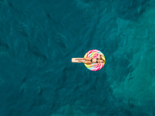 Aerial view of beautiful woman in bikini floating on inflatable lollipop mattress on Atokos island.
