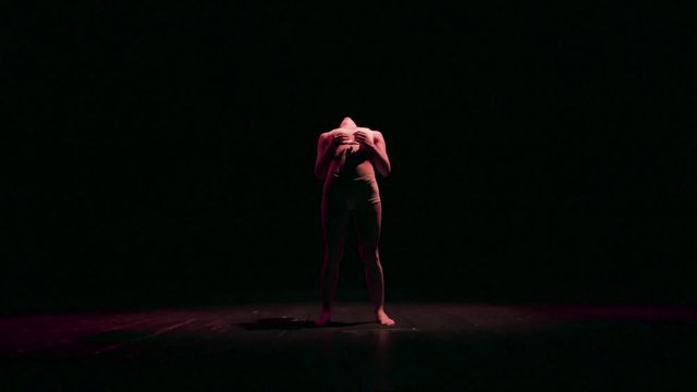 Female contortionist circus performer performing routine in dark studio