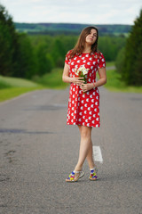 beautiful girl, brown hair, in a red dress holding flowers on the nature in the field and on the road, new faces