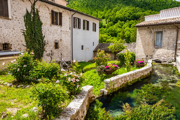 Fototapeta na wymiar The small village of Rasiglia, crossed by numerous streams and canals. A sluice regulates the flow of water. Well-kept garden full of flowers. Old brick houses. Foligno, Umbria, Italy