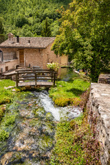 Naklejka premium The small village of Rasiglia, crossed by many streams and waterfalls, fed by the Menotre river. A sluice regulates the flow of water. A wooden bridge. Old brick houses. Foligno, Umbria.