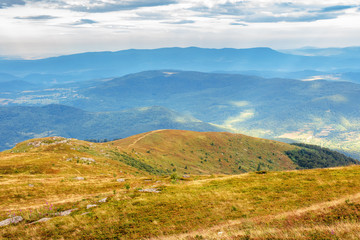 hills and meadows of carpathians in august. beautiful scenery on a cloudy day. boulders among the grass and overcast sky. dappled light in valley. mountain ridge in the distance