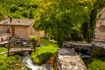 Fototapeta na wymiar The small village of Rasiglia, crossed by many streams and waterfalls, fed by the Menotre river. A sluice regulates the flow of water. A wooden bridge. Old brick houses. Foligno, Umbria.