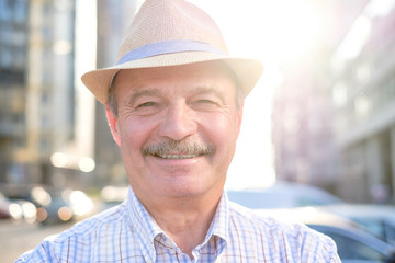 Retired senior hispanic man with hat standing and smiling at sunny day.