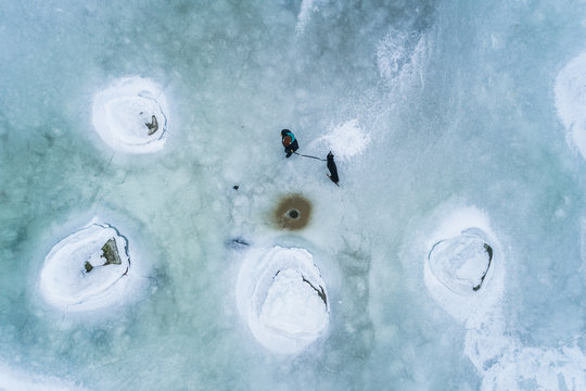 Aerial view of a man walking his dog on the frozen sea in Muraste, Estonia.