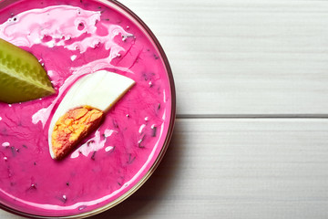 Bowl with cold beetroot soup with egg and cucumber on white table