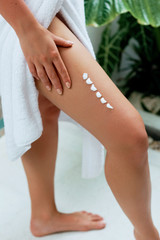 Woman hand is applying cream on leg skin from cellulite in spa. Beauty and Body care. Closeup on female hand apply moisturizing lotion on skin.