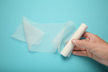 Doctor's hand is holding white gauze bandage on blue background. First aid, injury treatment.