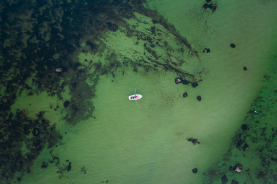 Aerial view of two people fishing in a small wooden boat in the middle of the green baltic sea in Estonia.
