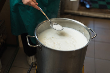 Cooking cottage cheese and cheese at home. Man creates cheese, heating milk and whey in an aluminum pan.