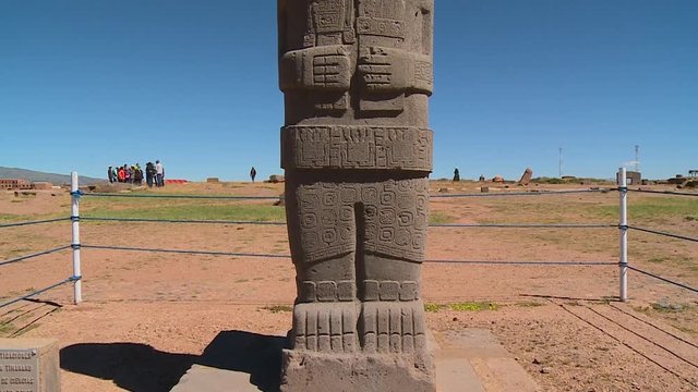 Close-up low angle lower part, tilting shot of string-fenced Ponce Monolith statue, with people visiting Tiwanaku on the background, La Paz, Bolivia