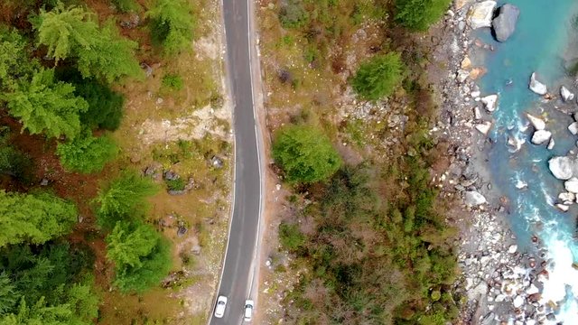 Drone video winding road in forest car moving and blue river on the side