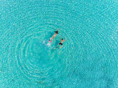 Aerial view of man and woman with masks and flippers diving in turquoise water.