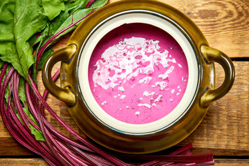Old vase with cold beetroot soup with young beets on  wooden table