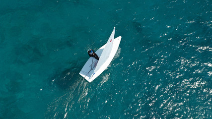Aerial photo of small sail boat operated by children in exotic tropical bay with turquoise sea