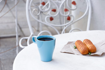 Aromatic coffee in a blue cup with eclairs in a summer cafe.