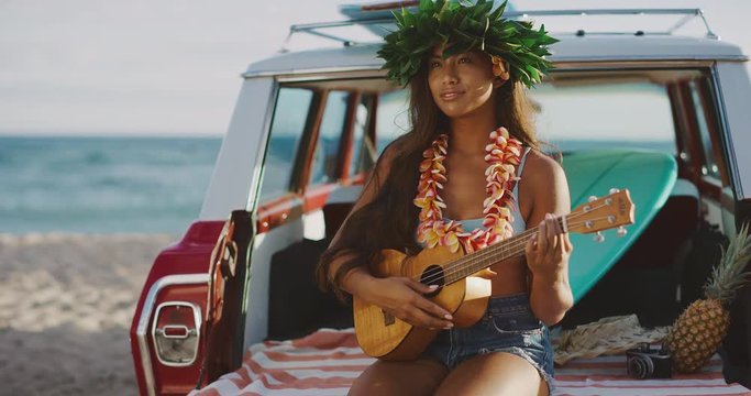 Portrait of beautiful young woman singing smiling and playing the ukulele, sitting in a vintage beach cruiser car at sunset, happy woman wearing flower lei and tiara, hawaiian island cruising