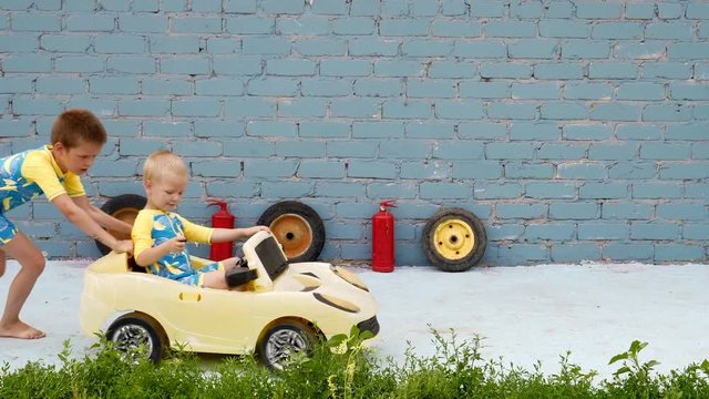 Funny kids in swimsuite roll their little brother on yellow car. Boys are happy together and dream of adventures, travels, exploits.