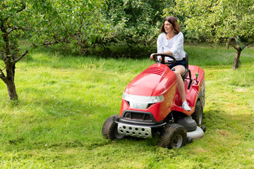 Woman in field garden job driving a lawn mower