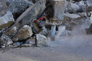 Backhoe with jackhammer tool breaking up concrete driveway.