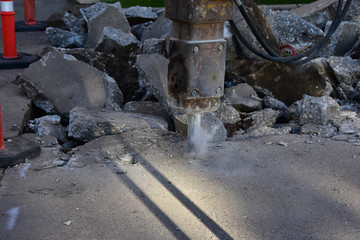 Backhoe with jackhammer tool breaking up concrete driveway.