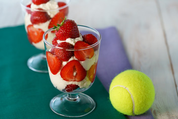 Whipped cream and strawberries served in a glass. Purple and dark green napkins, white wooden table, tennis ball, high resolution