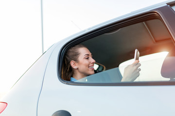 Young woman with smartphone on the back seat of a car